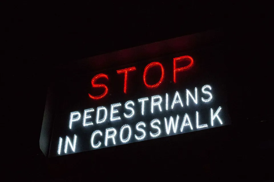 "Stop - Pedestrians in crosswalk" sign in white and red lights.